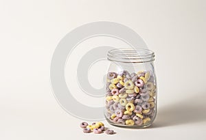 Sweet colorful cornflakes rings in a glass jar on a yellow background. Front view and copy space