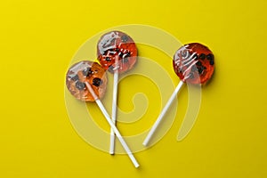 Sweet colorful lollipops with berries on yellow background, flat lay