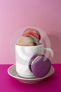 Sweet colorful macarons in white cup on pink background. Tasty red, green, brown, violet macaroons