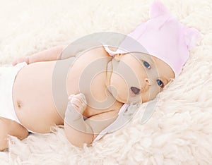 Sweet comfortable baby in hat yawns lying on the bed