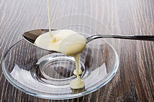 Sweet condensed milk in spoon above transparent saucer