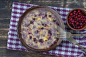 Sweet cottage cheese casserole with black currant and semolina on wooden table. Ceramic bowl with baked cottage cheese casserole