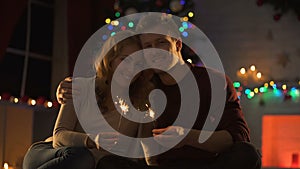 Sweet couple with Bengal lights sitting in cozy room near decorated X-mas tree