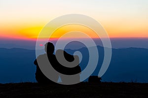 Sweet couple silhouette sitting on the mountain with sunset