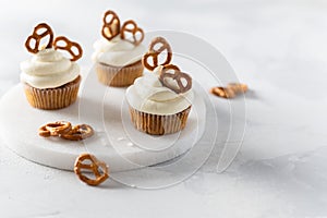 Sweet cupcakes with whipped cream and brezel on white marble tray. Bakery, confectionery banner, cookbook recipe, menu. Side view