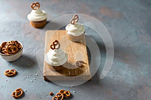 Sweet cupcakes with whipped cream and brezel on wooden board. Bakery, confectionery banner, cookbook recipe, menu. Side view, copy