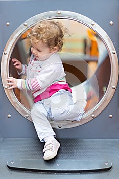 Sweet curly baby girl sliding on a playground