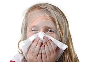 Sweet and cute blond hair little girl blowing her nose with paper tissue having a cold feeling sick