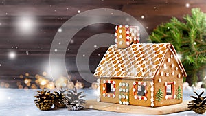 Sweet decorated gingerbread house closeup with pine cones decorations, fir tree branches, bokeh and snowfall. Christmas card with