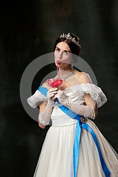 Sweet delight. Elegant woman, royal person, queen or princess in white medieval outfit tasting jelly candy on dark