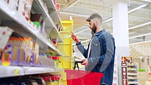 sweet department in supermarket, man is choosing chocolate, reading labels