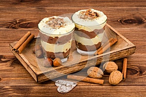 Sweet dessert - chocolate and vanilla pudding in glasses served on the wooden tray with nuts and cinnamon sticks.
