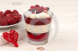 Sweet dessert in glass with cream, jell, raspberries and blueberries on wooden background.