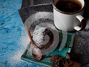 Sweet dessert time. Chocolate delicious muffin with powdered sugar. Mug of black tea and milk chocolate.