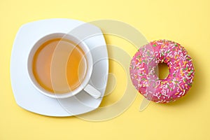 Sweet donut with icing in and a cup of tea on a yellow background