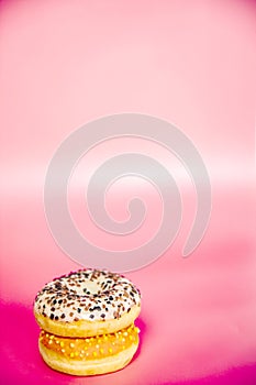 Sweet donuts stacked in a stack on a pink background. Copy space, various glaze and sprinkels chocolate chip, snack fast