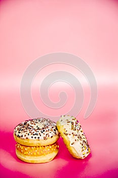 Sweet donuts stacked in a stack on a pink background. Copy space, various glaze and sprinkels chocolate chip, snack fast