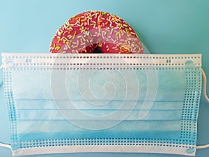 Sweet doughnut in pink icing on a blue background in a medical mask. Love in quarantine, self-isolation.