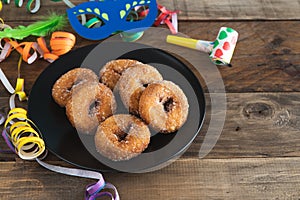 Sweet doughnuts on a black plate on a wooden background with typical carnival decorations. Copy space