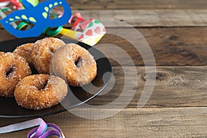 Sweet doughnuts on a black plate on a wooden background with typical carnival decorations. Copy space