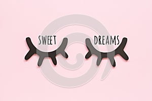 Sweet dreams text and decorative black wooden eyelashes, closed eyes on pink background. Concept Good night. Top view Copy space