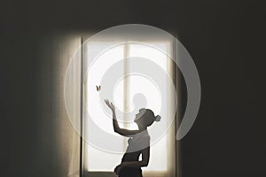 Sweet encounter between a butterfly and a girl illuminated by the light of a window