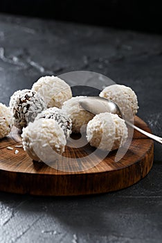 Sweet energy balls with coconut flakes in pile on dark oak slab with silver spon on black background photo