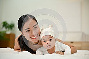 Sweet family moment. Young Asian mom lay down with her baby, smiling to camera