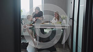 A sweet family of mother and two daughters drink tea in the kitchen in the morning - their pet dog and cat lying on the