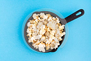 Sweet fast food. Caramel popcorn in a cast iron pan on a blue background. Top view