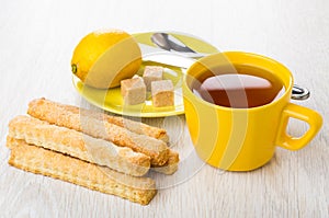 Sweet flaky sticks, tea, teaspoon, lemon, sugar, knife on saucer