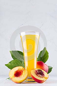 Sweet fresh yellow juice of peach and red nectarines with green leaves, juicy half cut on white wood table, vertical.