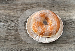 Sweet fried donut covered with sugar on plate on the old wooden background