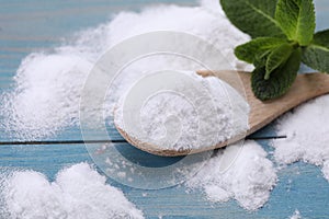 Sweet fructose powder, spoon and mint leaves on light blue wooden table, closeup