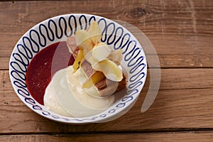 Sweet fruit dessert with delicious gruit and milk sauce served in a white bowl over rustic wooden table background.