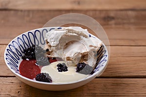 Sweet fruit dessert with delicious gruit and milk sauce served in a white bowl over rustic wooden table background.