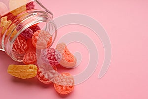 Sweet fruit hard candies pouring out of the glass mason jar on colored pink background. Overhead view of colorful caramel