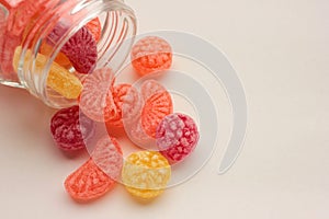 Sweet fruit hard candies pouring out of the glass mason jar on white background. Overhead view of colorful caramel assortment.