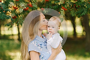 Sweet and gentle young woman a European mother holds her little son in her arms and kisses him near the branches with red Rowan