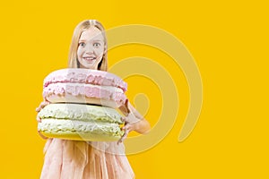 Sweet gift. A cute girl is holding two huge macaroons on a yellow background. Round dessert. Christmas sweetness