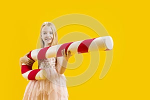 Sweet gift. Large lollipop. Christmas sweetness. A cute girl is holding a huge red and white candy on a yellow background