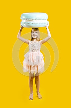 Sweet gift. Round dessert. Christmas sweetness. A cute girl holds a huge blue macaroons above her head on a yellow background