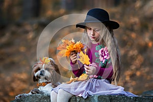 Sweet girl in a hat weaves wreath of autumn maple leaves
