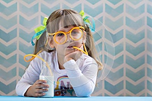 Sweet girl kid drinking milk with funny glasses straw.