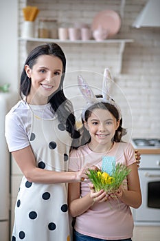 Sweet girl wearing easter bunnys ears standing near her mom and smiling happily