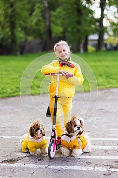 Sweet girl in a yellow dress katatsya scooter with dogs in the park