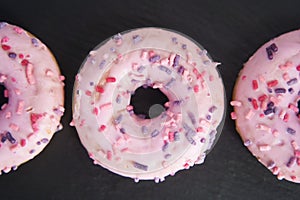 sweet glazed pink donuts close-up on a black tray.