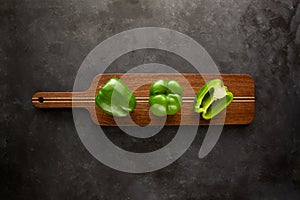 Sweet green peppers on wooden cutting board on black and dark grey background. Green pepper sliced and chopped on wooden chopping