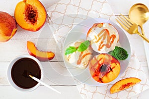Sweet grilled peaches with vanilla ice cream and caramel sauce, above view table scene over white wood