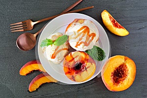 Sweet grilled peaches with vanilla ice cream and caramel sauce, top view table scene on slate